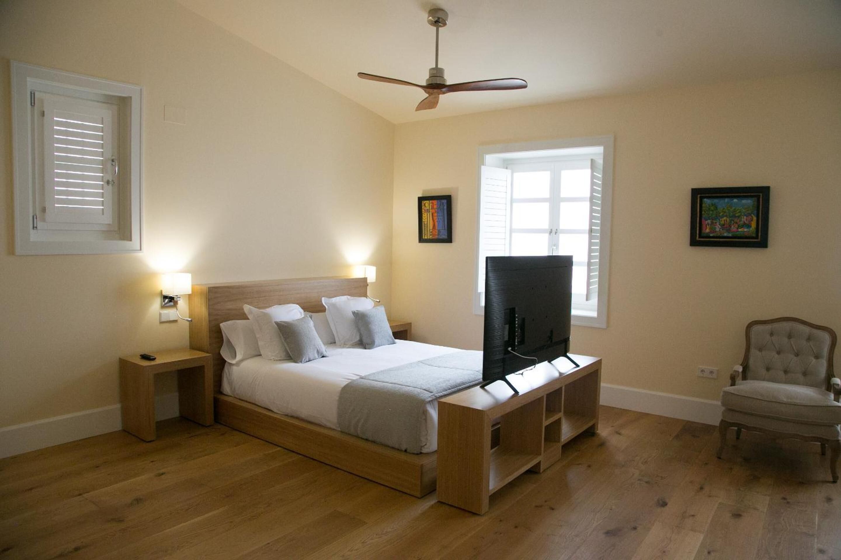 A bedroom with a bed, a television, a chair, and a ceiling fan.