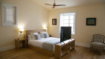 A bedroom with a bed, a television, a chair, and a ceiling fan.