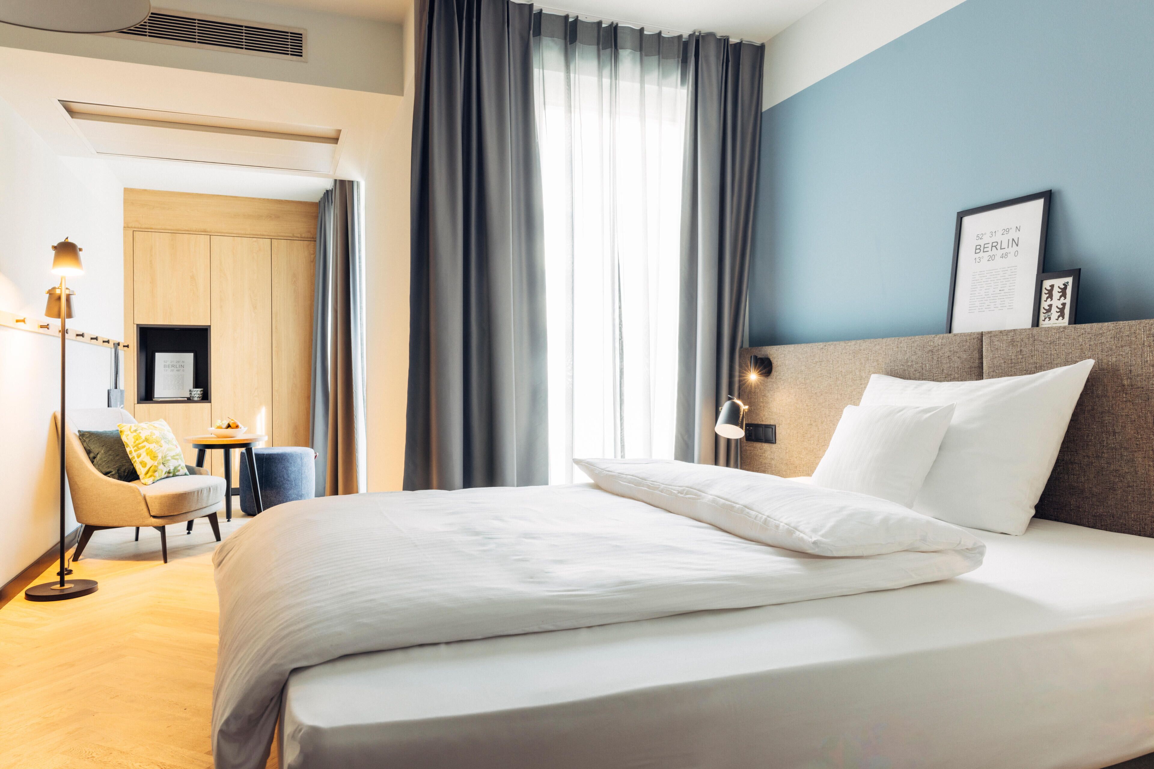 A hotel room with a bed, a desk, a chair, and a large window with curtains.