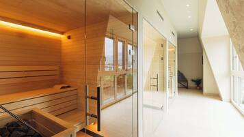 Un spa moderno con paneles de madera, una pared de vidrio y una sauna con piedras a la vista.
