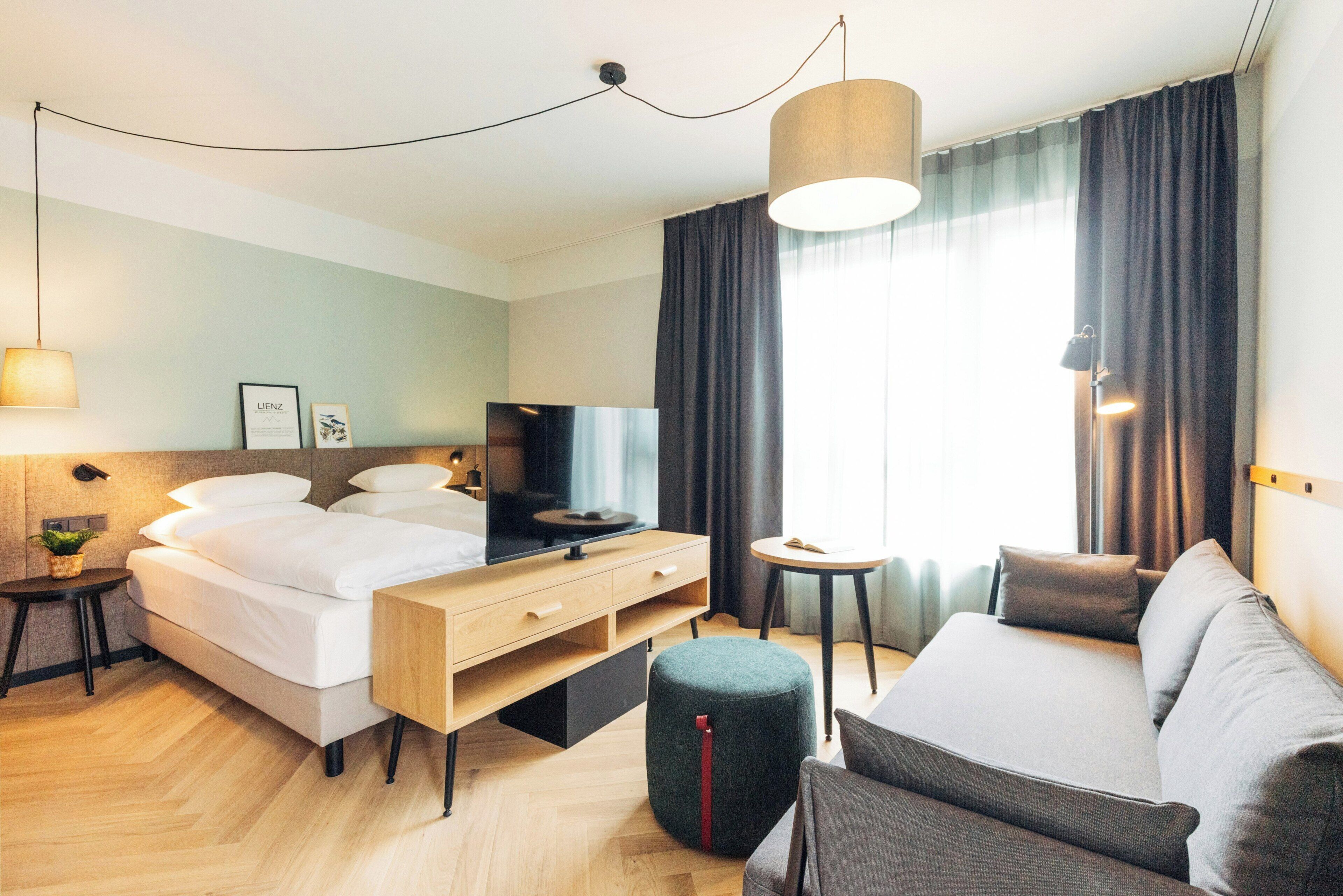 A modern hotel room with a bed, sofa, TV, and a small table.