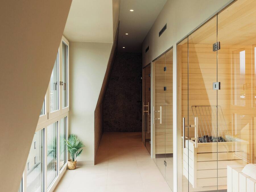 A modern hotel corridor with a glass wall, a staircase, and a potted plant.