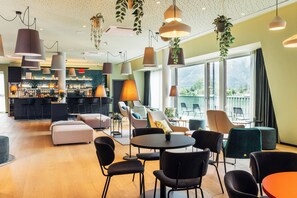 A modern lounge area with seating, a bar, and large windows offering a view. - Harry s Home Lienz (Lienz)