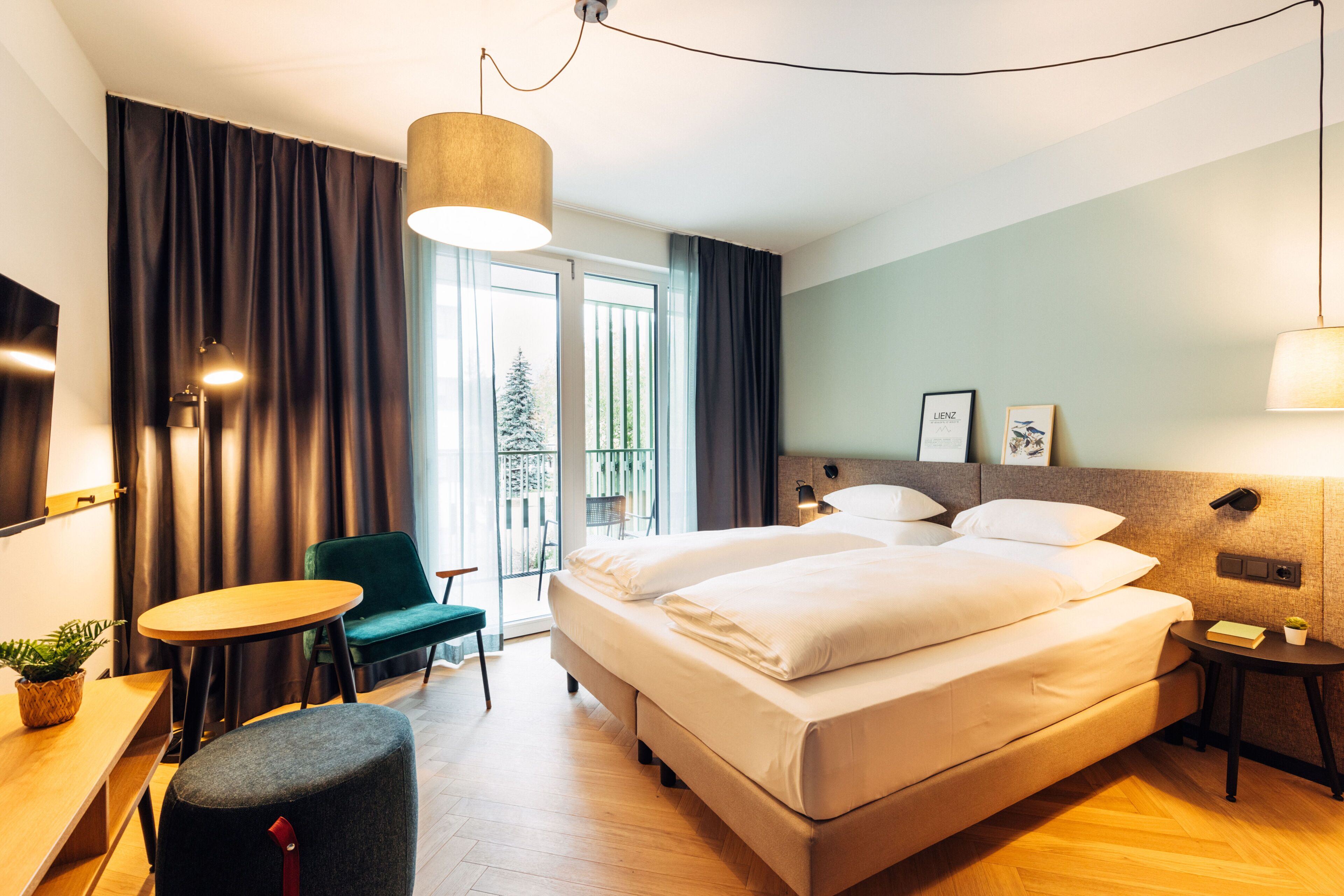 A hotel room with a large bed, a desk with a chair, a small table, and a potted plant.