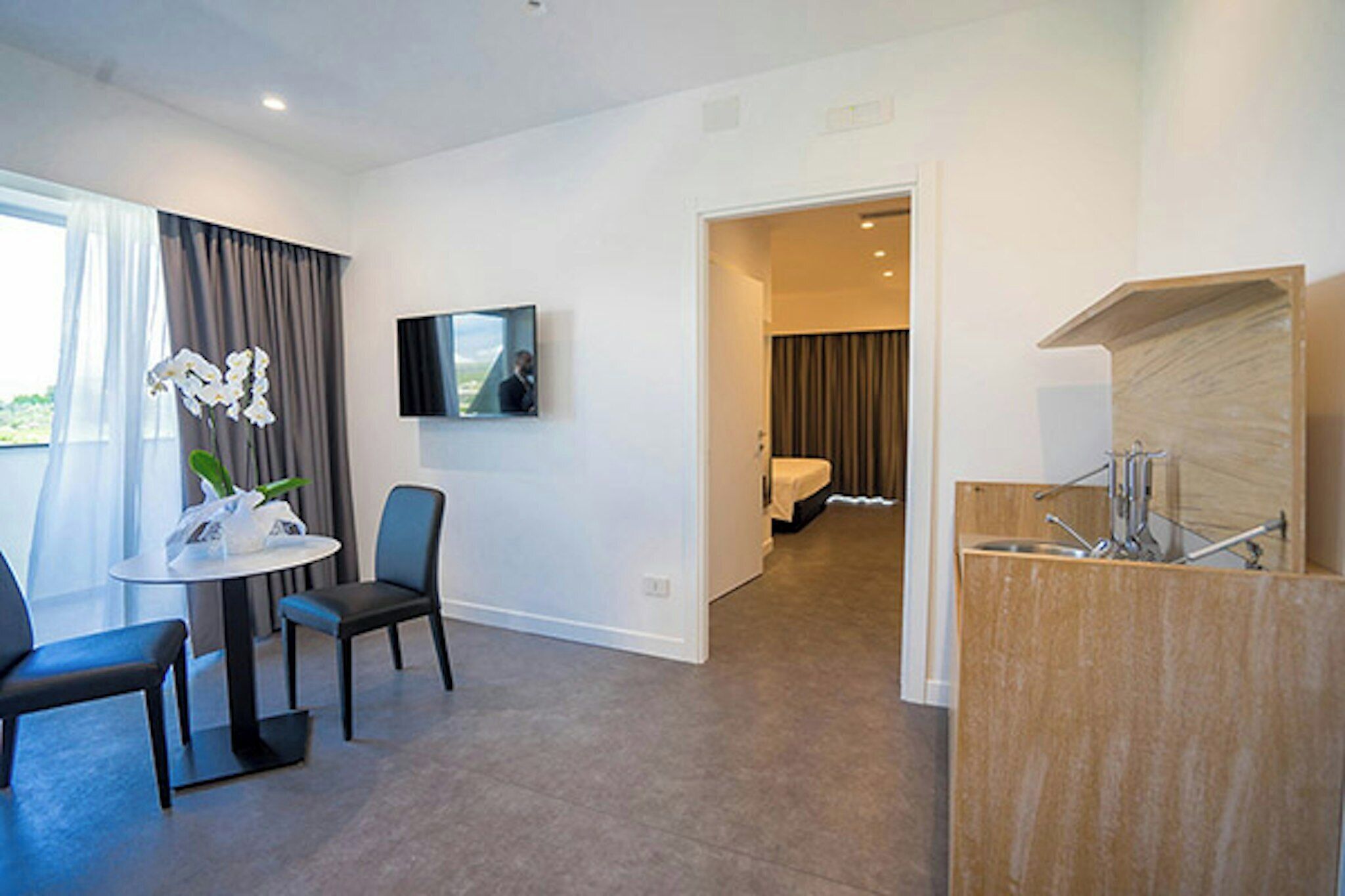 A hotel room with a dining area, a bed, a TV, and a bathroom.