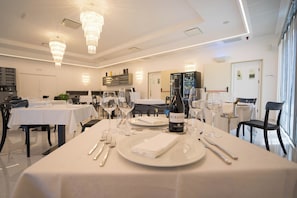 A dining area with tables set for a meal, a bottle of wine, and a kitchen in the background. - Pm Hotel (Catanzaro)