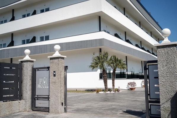 Un hotel moderno con fachada blanca, varios balcones y entrada protegida por una reja.