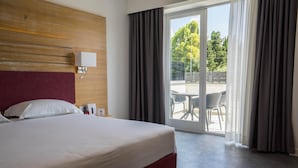 A hotel room with a large bed, a wooden headboard, a bedside table with a lamp, and a view of the outdoors through a sliding glass door. - Pm Hotel (Catanzaro)