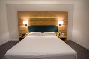 Habitación de hotel con una cama grande, cabecera de madera, lámparas de noche y un teléfono en la mesita.