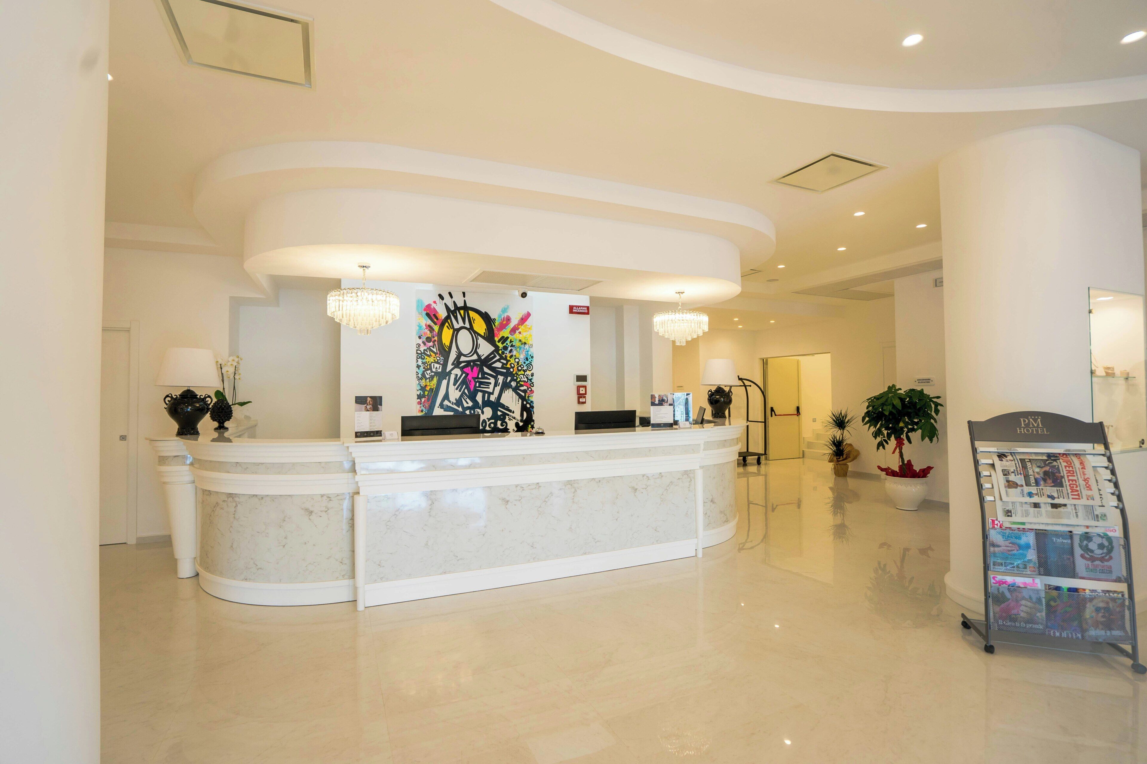 Zona de recepción de un hotel con un mostrador de mármol, un cuadro abstracto de gran tamaño y una lámpara de araña.