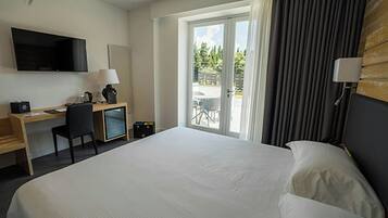 Et hotelværelse med en stor seng, et skrivebord med stol, et fjernsyn ophængt på væggen og en skydedør til et udendørs område.