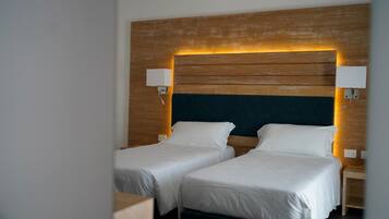A hotel room with two single beds, wooden headboard, bedside lamps, and a dark-colored headboard.