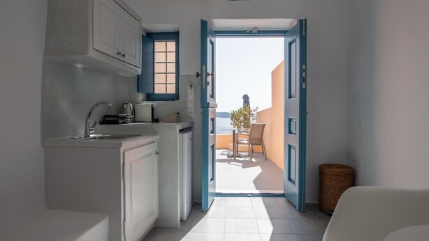 A narrow kitchen with white cabinets and a view to an outdoor balcony. - Horizon Aeifos (Santorini)