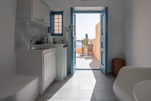 A narrow kitchen with white cabinets and a view to an outdoor balcony. - Horizon Aeifos (Santorini)