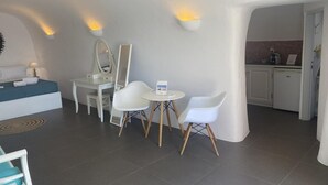 A modern hotel room with a bed, a desk, two chairs, a small table, and a mirror. - Horizon Aeifos (Santorini)