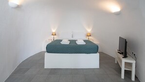 A modern bedroom with a bed, two bedside lamps, a TV, and a small table. - Horizon Aeifos (Santorini)