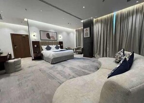 A modern hotel room with a large bed, a sofa, a desk, and a chair. - Sunday Luxury Central Formerly Anan Hotel (Riyadh)