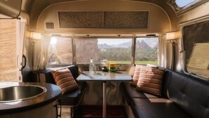 Interior compacto de una caravana con kitchenette, zona de estar y ventanas amplias que ofrecen vistas panorámicas.