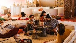 Un grupo de personas sentadas sobre una alfombra en una habitación tipo tienda, con sofás y una mesa.