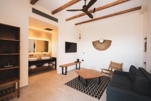 A modern living room with a dark sofa, a wooden coffee table, a patterned rug, a woven wall hanging, and a bench. - Kouros Blanc Paros (Paros)