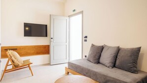 Habitació moderna amb un sofà gris, una cadira de fusta, una taula rodona de fusta i un televisor de pantalla plana fixat a la paret.