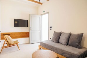 Ett modernt rum med en grå soffa, en trästol, ett runt träbord och en platt-TV som är monterad på väggen.