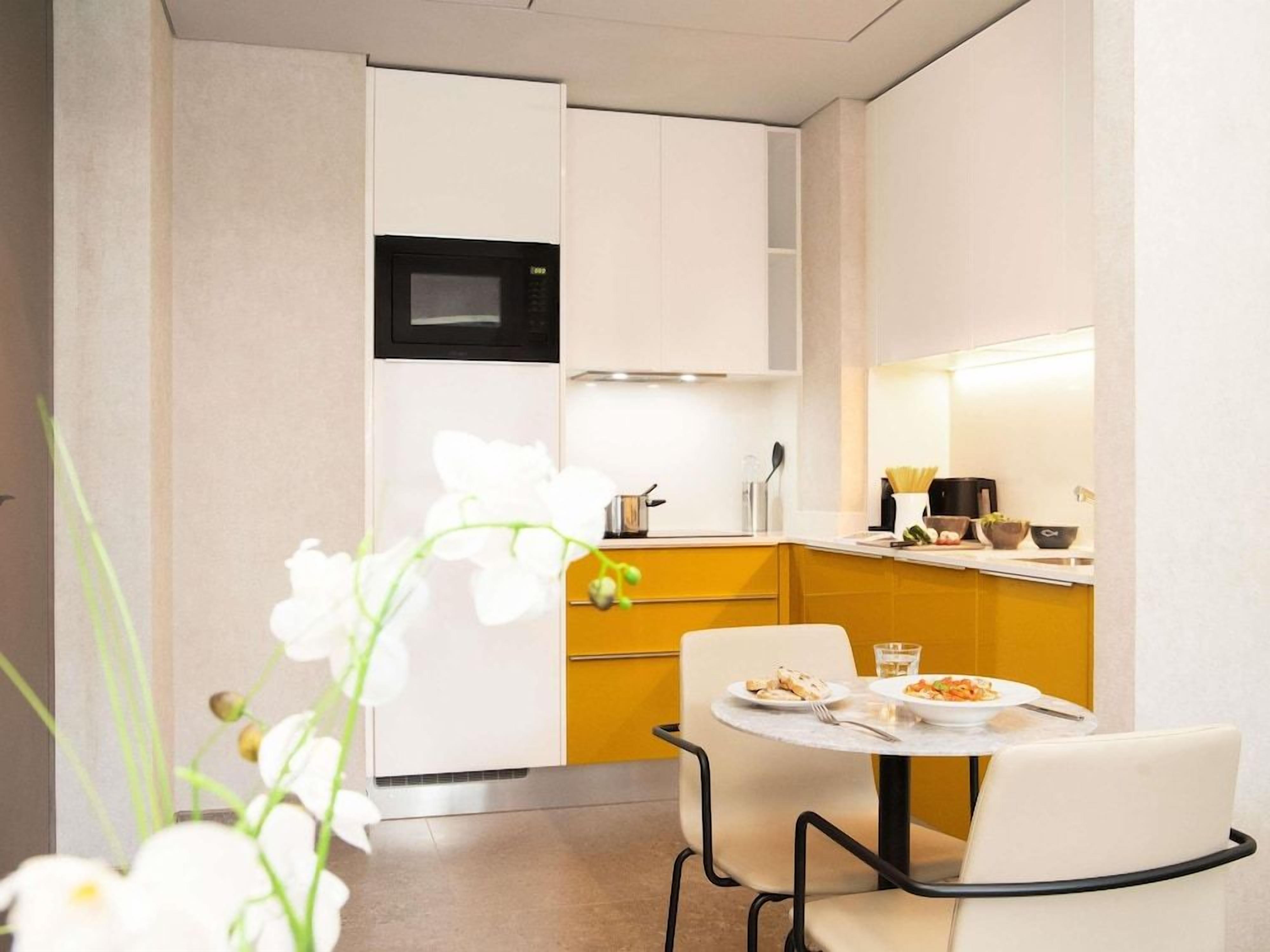 A compact kitchen with a microwave, a small dining table with chairs, and a yellow accent wall.