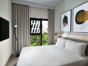 A modern hotel room with a large bed, a TV mounted on the wall, and a window with curtains. - Adagio Apart Hotel (Abidjan)