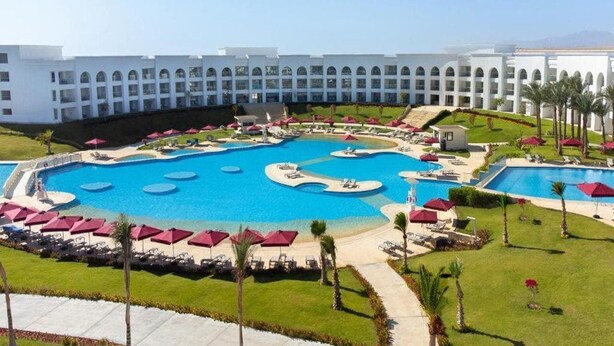 A large, multi-level swimming pool complex with multiple pools and sunbathing areas, surrounded by a white building with arched windows. - Rixos Radamis Sharm El Sheikh (Sharm El Sheikh)