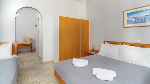 Una habitación de hotel con una cama, un armario de madera, un banco y un cuadro en la pared.