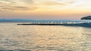 A beach with a pier extending into calm waters, rows of beach chairs, and a distant mountain range. - Stefania Beach Resort (Eretria)