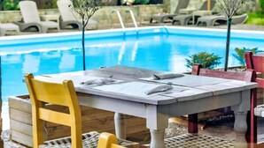 Un área de comedor junto a la piscina con una mesa, sillas y sillones de descanso al fondo.