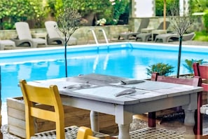 A poolside dining area with a table and chairs, a pool, and lounge chairs in the background. - Stefania Beach Resort (Eretria)