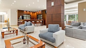 A modern living room with a sofa, armchairs, and a coffee table. There is a kitchen area with bar stools and a counter. - Stefania Beach Resort (Eretria)