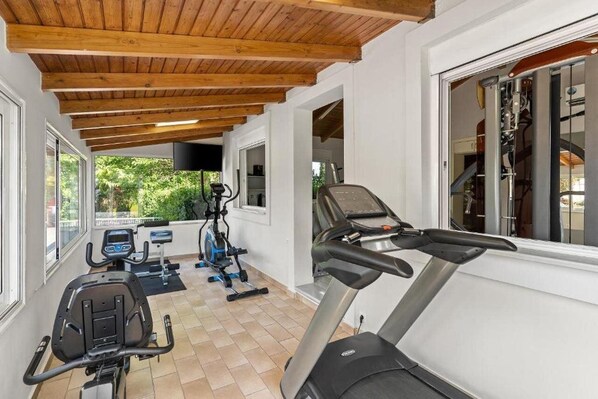 A covered outdoor gym area with exercise equipment, large windows, and a view of greenery. - Stefania Beach Resort By Anayia All Inclusive Resorts (Eretria)