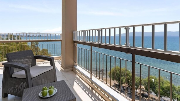 A balcony with a view of the sea, a wicker chair, a small table with apples, and a railing. - Stefania Beach Resort (Eretria)