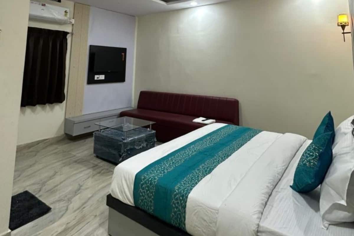 A hotel room with a bed, a red sofa, a glass coffee table, and a TV on the wall.