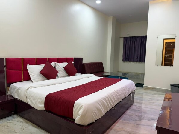 A modern bedroom with a large bed, a nightstand, a glass table, and a view of a bathroom.