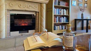 A cozy reading area with a fireplace, bookshelves, and a bottle of liquor. - Hotel Finca Malvasia (Cabezon de Liebana)