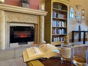 A cozy reading area with a fireplace, bookshelves, and a bottle of liquor. - Hotel Finca Malvasia (Cabezon de Liebana)