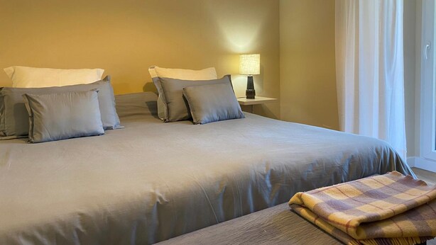 A bedroom with a large bed, two bedside tables, a lamp, and a window with curtains. - Hotel Finca Malvasia (Cabezon de Liebana)