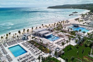 An aerial view of a resort with multiple swimming pools, beach access, and palm trees.