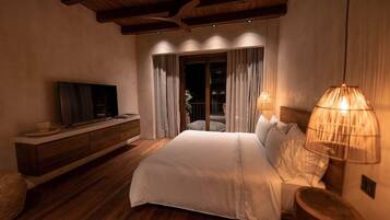 A bedroom with a large bed, wooden flooring, a TV on a wooden console, and a balcony with curtains.