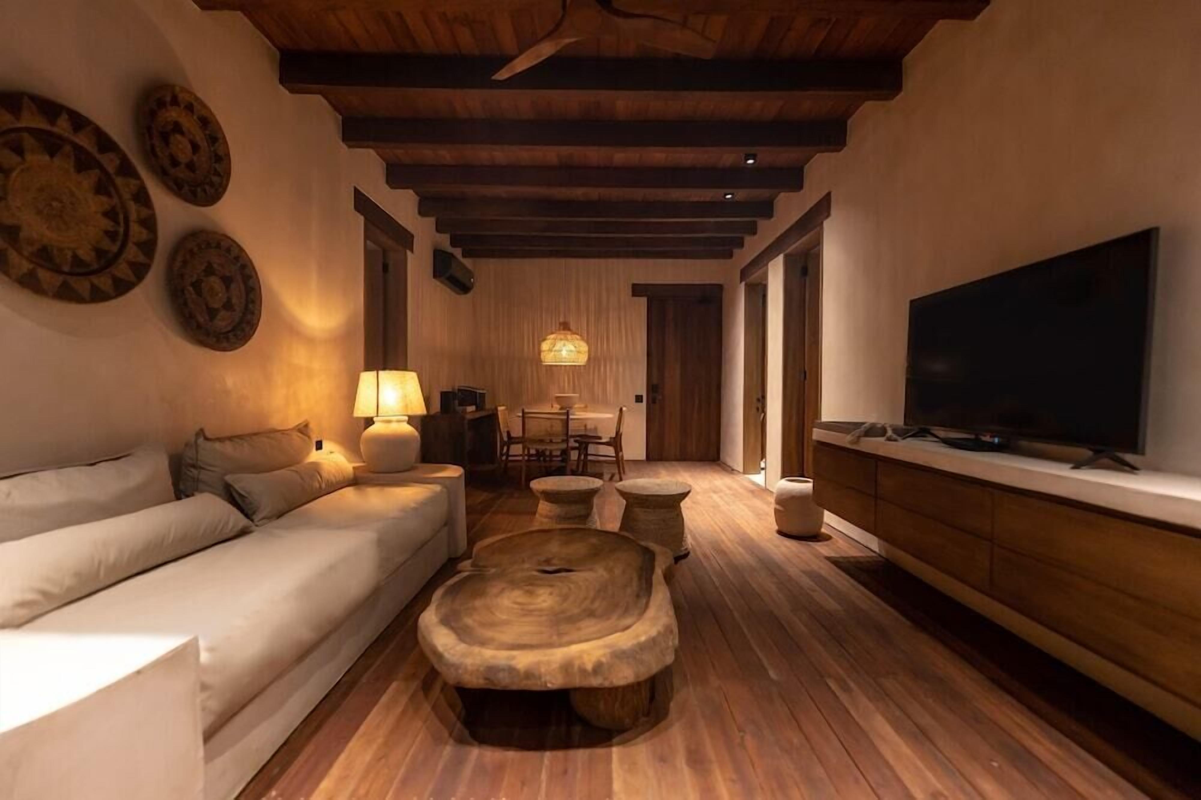 A cozy living room with a wooden ceiling, a sofa, a coffee table, a TV, and a dining area with chairs and a table.