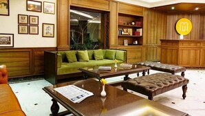 Un salon spacieux avec un canapé vert, des poufs en cuir, une table basse en bois et une bibliothèque.