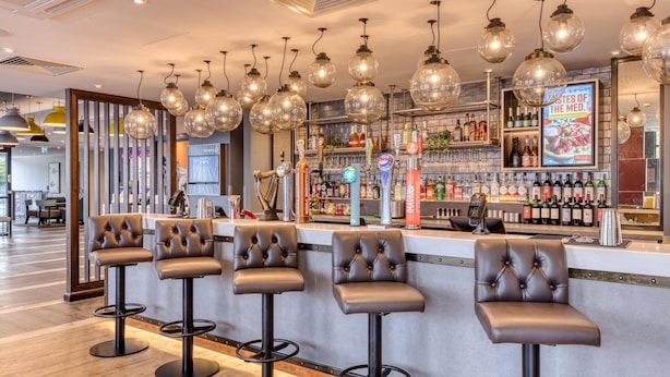 A bar area with leather barstools, a well-stocked liquor shelf, and hanging glass globes. - Premier Inn York City Centre (York)