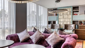 A modern living room with a purple sofa, a round coffee table, and a large bookshelf filled with books. - Premier Inn York City Centre (York)