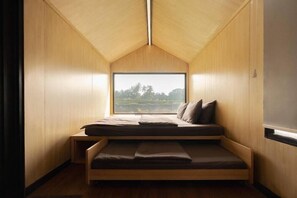 A compact, triangular room with a bed and a large window offering a view of a landscape. - Bobocabin Ubud, Bali (Tegallalang)