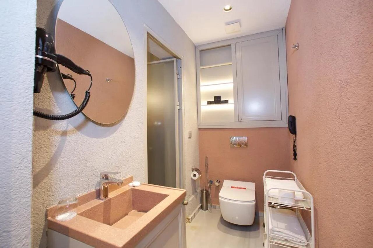 A compact bathroom with a sink, toilet, and a small shelf with toiletries.