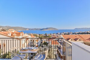 A balcony with a table and chairs, overlooking a coastal town with buildings and the sea. - Sole Suites (Kaş)
